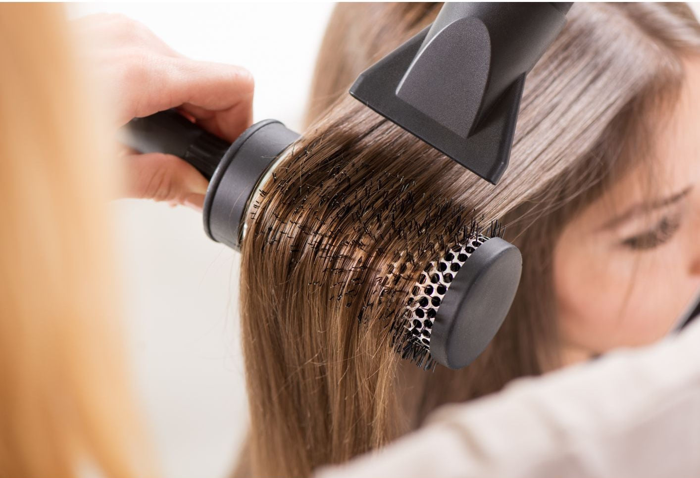 Person using a hair straightening tool on their hair with a white background